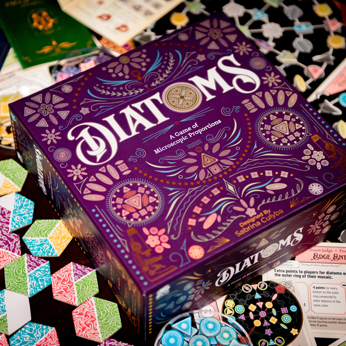 Diatoms board game box with colorful algae art tile components spread around it – award-winning tile placement game for 1–4 players