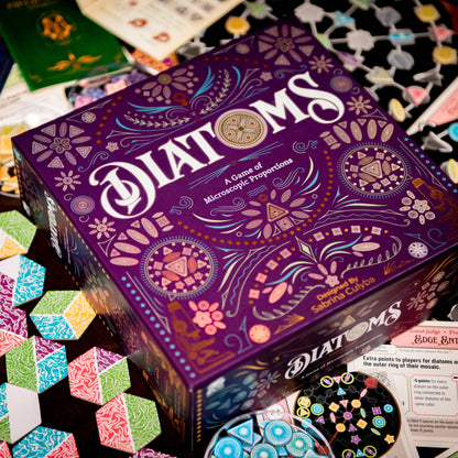 Diatoms board game box with colorful algae art tile components spread around it – award-winning tile placement game for 1–4 players