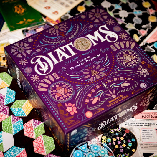 Diatoms board game box with colorful algae art tile components spread around it – award-winning tile placement game for 1–4 players